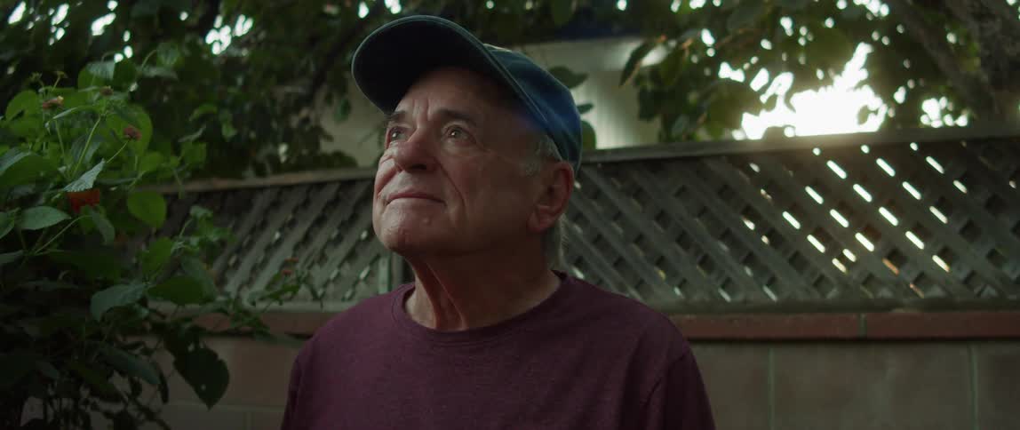 A smiling elderly man sitting on a bench in the backyard