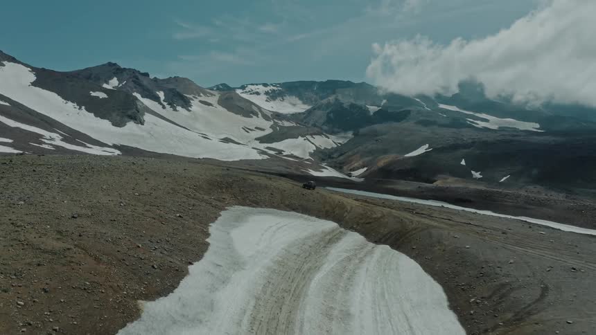 A black car driving through a landscape of hills and mountains during winter