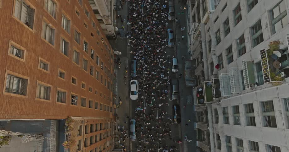 Aerial view of a crowd of people walking in the center of a street surrounded by residential buildings