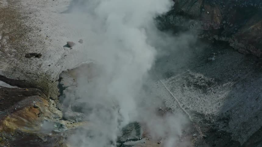 Aerial into a rocky mountain crevasse filling with smoke escaping from the ground below