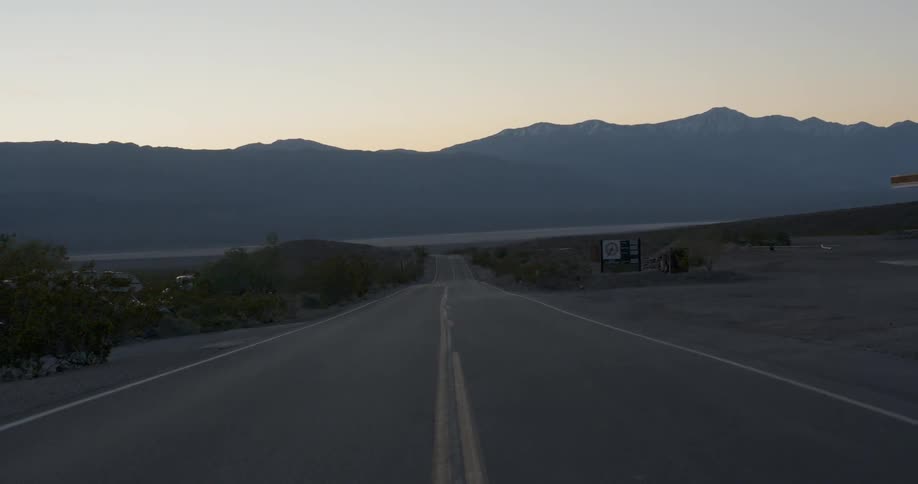 An empty road leads towards a mountain range
