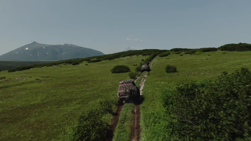 Aerial view of jeeps driving on the hills next to the mountains