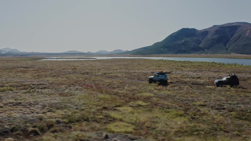 Aerial panorama of two jeeps driving through a terrain in the grassland beside mountains in the morning