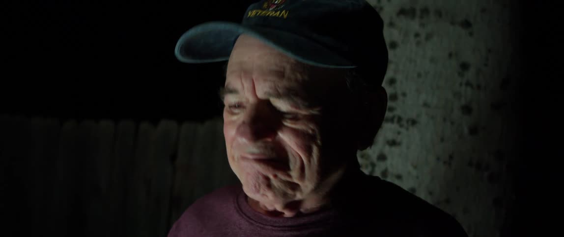 Elderly man wearing a baseball cap at night looks down