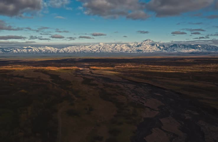 Aerial timelapse of a grassland with snow mountains on the horizon