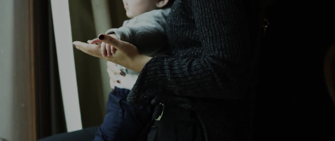 A woman holding hands with a baby leaning against her to stay standing up