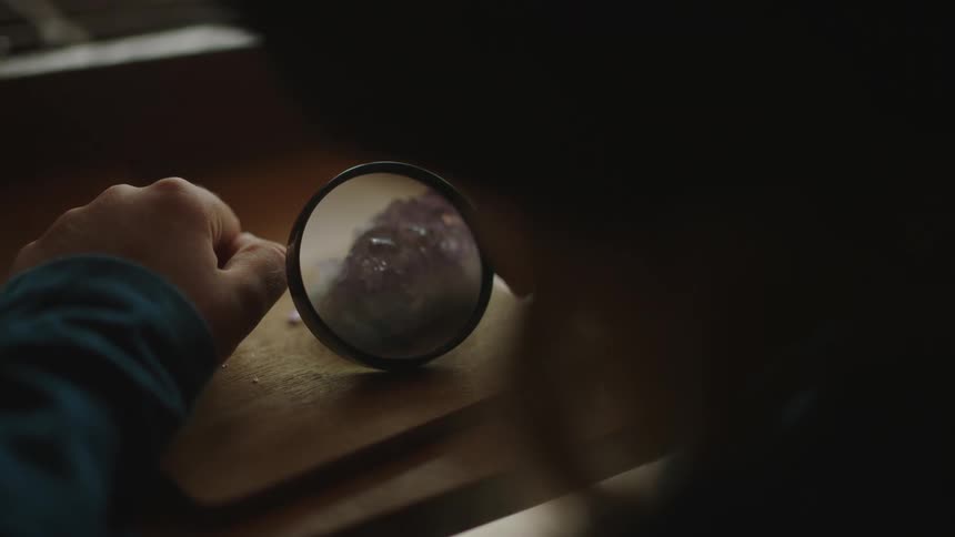 Closeup of a boy holding a magnifying glass and examining a precious stone