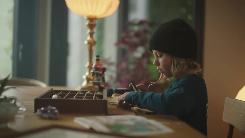 Boy sitting at the home table and examining stones with a magnifying glass