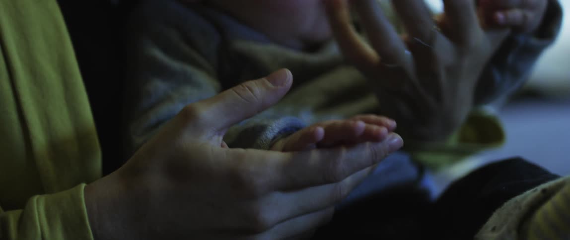 Closeup of the mothers hands holding those of her baby in her lap