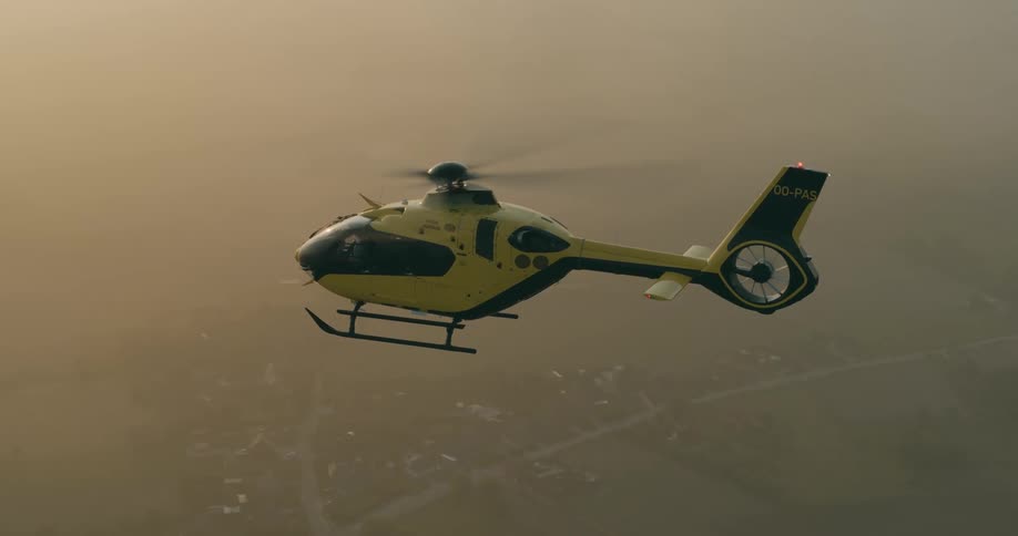 Aerial view of a yellow and black helicopter in flight during hazy weather conditions over a city