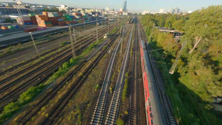 Aerial view of a train passing by the side of a port with containers and vegetation