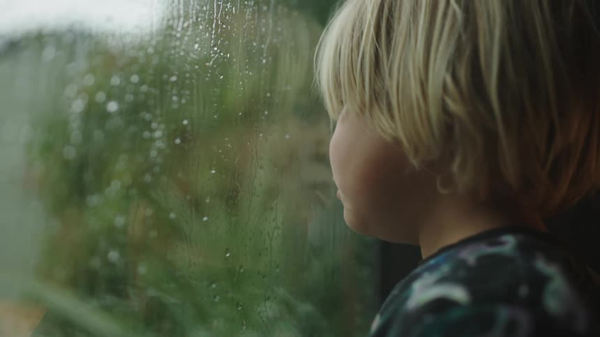 A child is watching the rain through the window