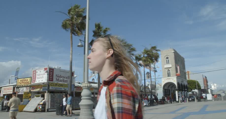 A woman stands near some shops on a windy day