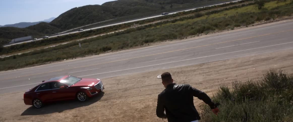 A man jumps down a hill running towards a car