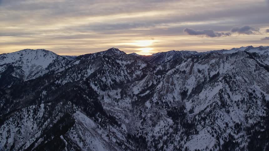 Snow covered mountain range with the sun shining through clouds on the horizon