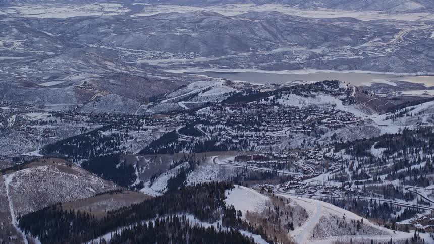 Road winds over conifer and snow covered mountains through town near lake in winter