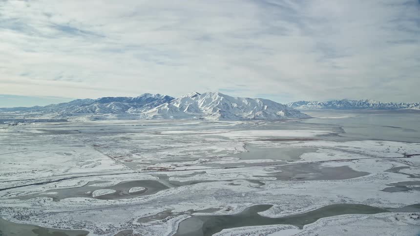 Snowy landscape with winding frozen rivers leading towards a mountain range under a cloudy sky