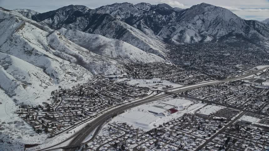Aerial over snow covered single family home neighborhoods beside snow covered mountains