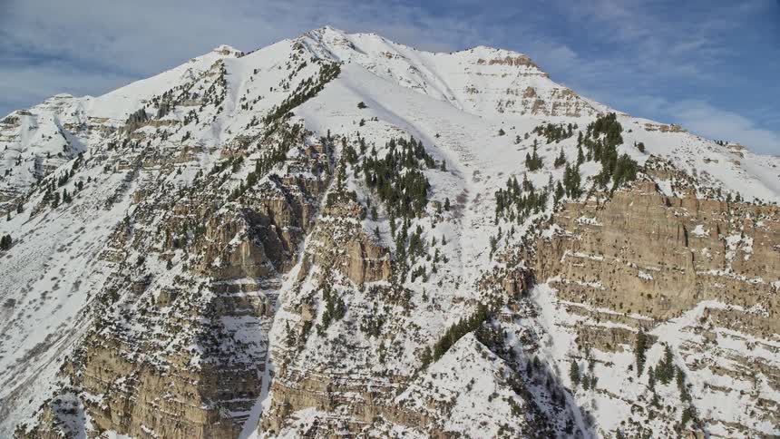 Aerial view of a snowcovered mountain with exposed rocky cliffs and scattered coniferous trees