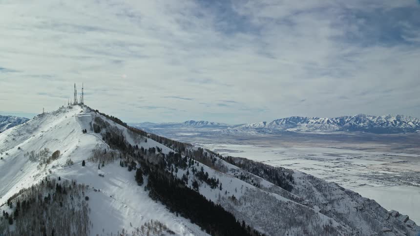 Aerial of farnsworth peak covered in snow on a bright day with mountians and cloudy blue sky in the background
