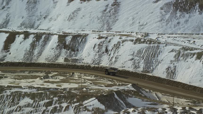 A truck drives down a dirt road next to a snowcovered mountain