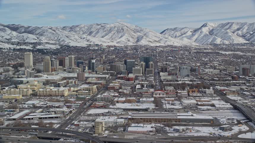 An aerial perspective reveals a snowy downtown area nestled within the city with distant mountains forming a picturesque backdrop