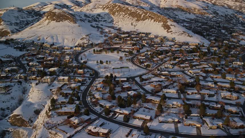 Aerial panorama of a residential neighborhood next to mountains all covered in snow under a morning sky