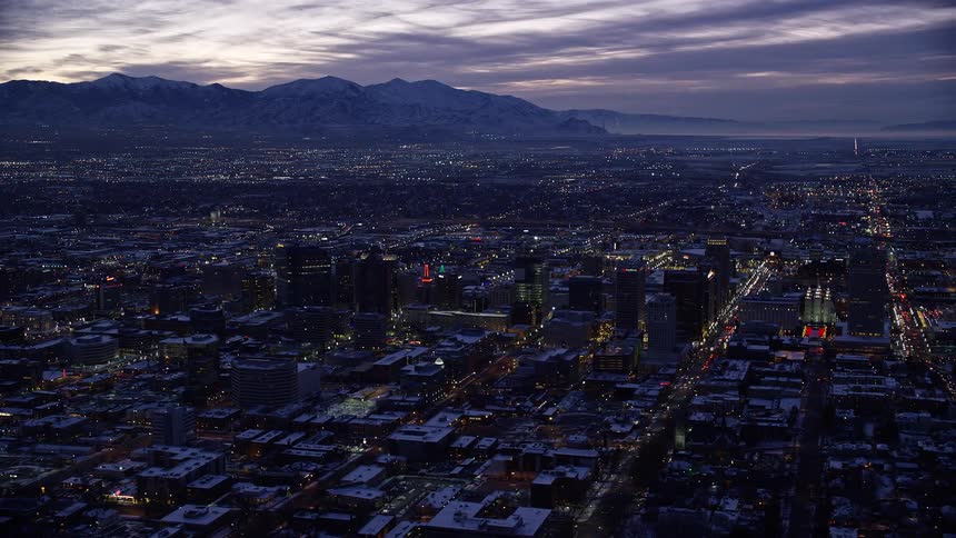 Aerial of a city with snowy buildings with mountains in the background just after sunset