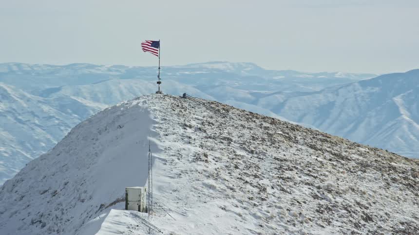 An american flag waving in the wind at the top of a mountain