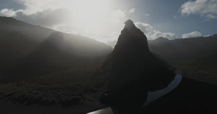 Bright glaring sun casts rock formations between mountain and river into silhouette