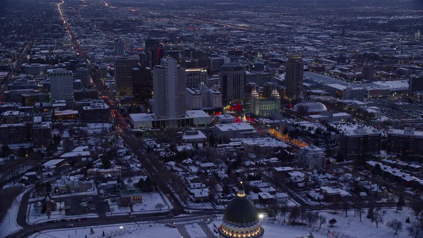 Aerial of downtown salt lake city in utah over the capital building and temple square lit up with red and gold lights at dusk in the winter with mountains on the horizon