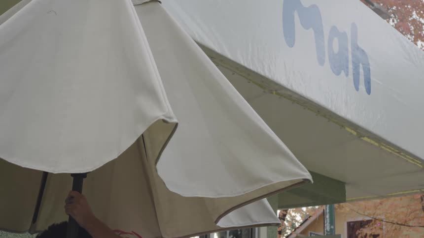 Man closing a parasol outside a neighborhood corner convenience store