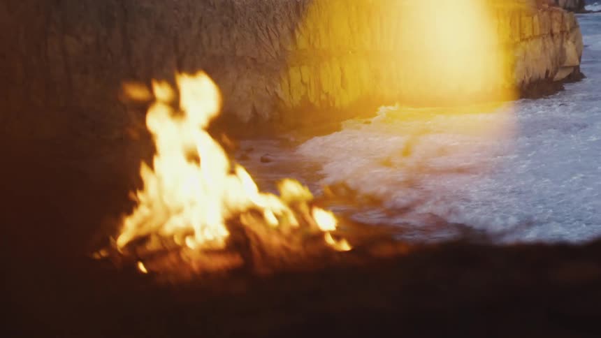 A person walks by the campfire by the shore