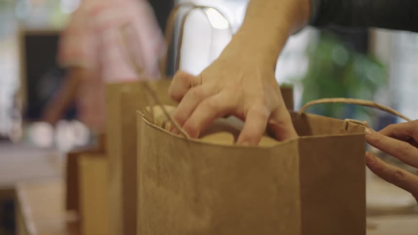 A person putting groceries into a paper bag