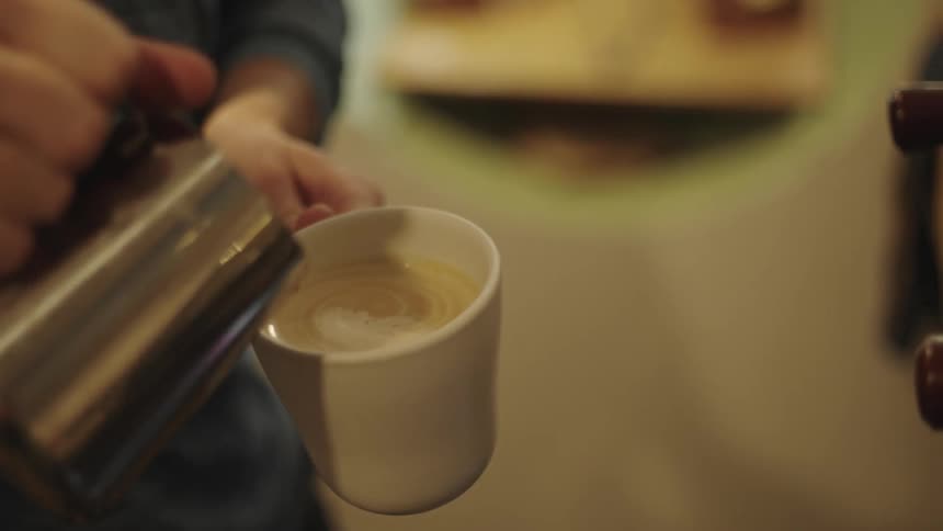 A person pouring coffee into a white mug using a teapot