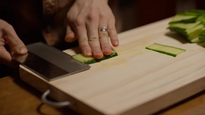 A persons hands chopping vegetables on a wooden cutting board using a cleaver knife
