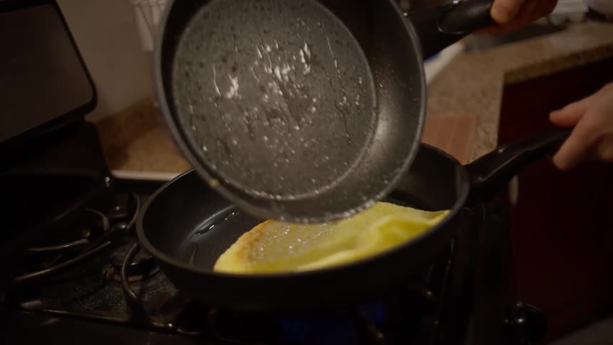 Omelete being placed into another pan on the stove