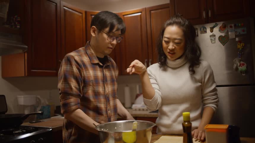 Two people are adding salt and seasoning food in a pan