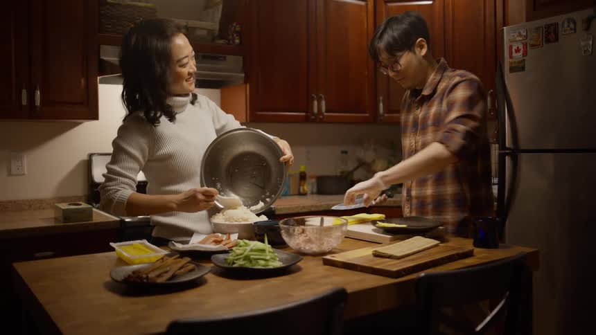 Woman spoons rice into bowl while man chops ingredients for dinner