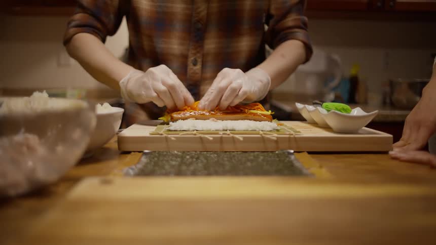 Hands in gloves preparing a sushi roll