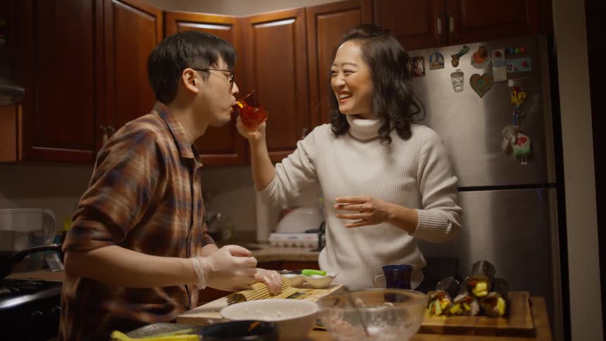 A woman helps a man drink tea while preparing food