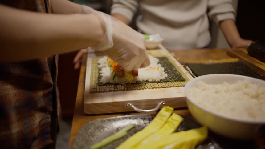 Two people preparing sushi rolls