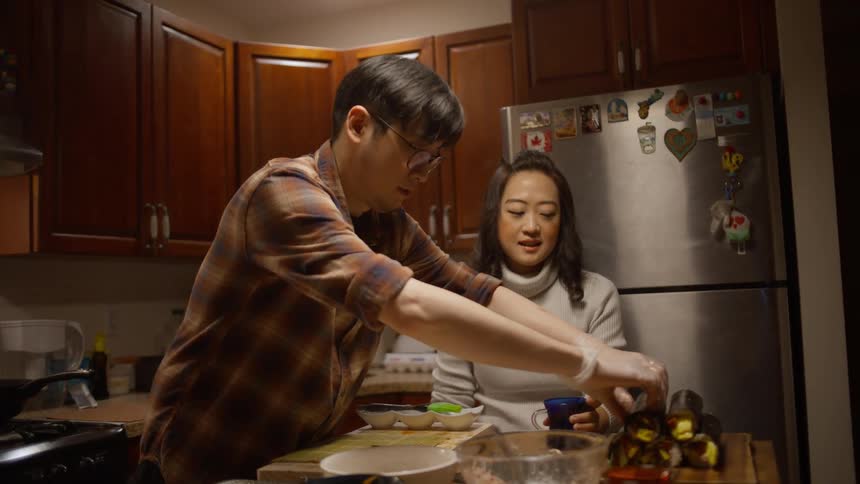A man prepares a Korean meal while talking to a woman in the kitchen