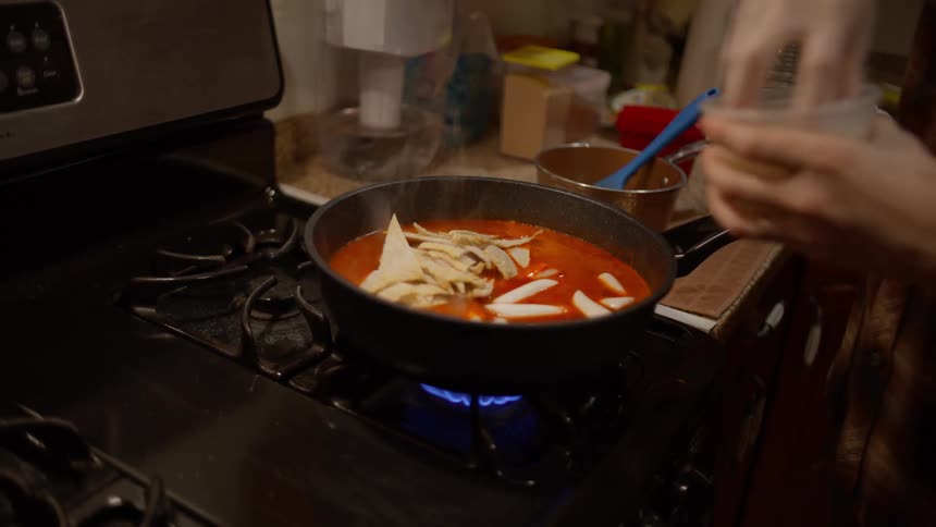 Closeup of a man putting rice cakes into sauce in the pot on the stove