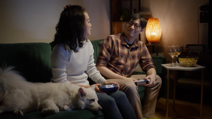 A couple enjoying video games together seated on the couch alongside their dog