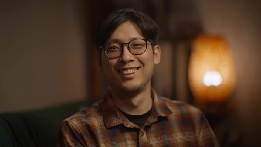 A sitting man wearing glasses suddenly laughing