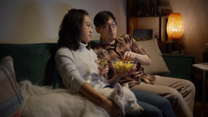 A man and a woman eating popcorn while watching a movie