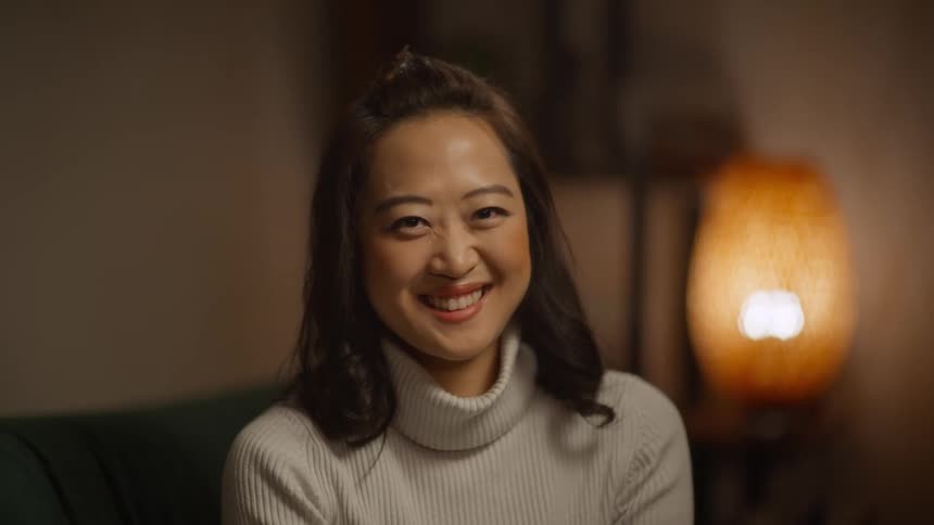 Woman with a white turtleneck sweater sits on couch in the living room laughing