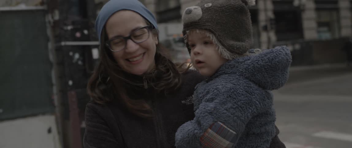 A woman is holding a baby and smiling in a city