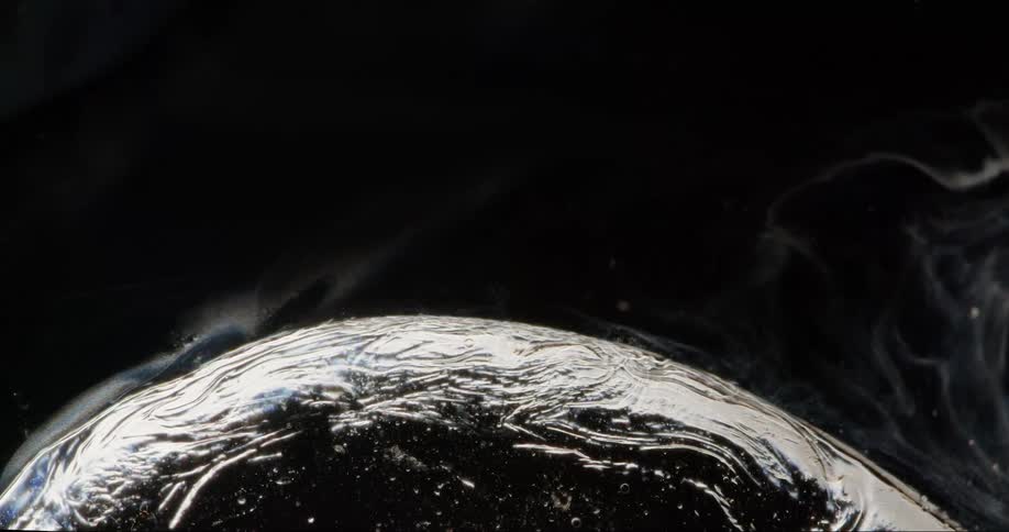 Rippling surface of a water bubble against a black background